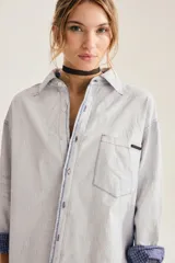 Camisa oversize de algodón con textura de cuadrillé sutil, cuello clásico, bolsillo frontal y mangas largas con puños vueltos que revelan un forro interior a cuadros.