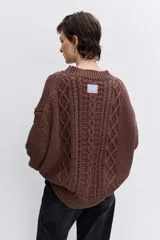Sweater de punto color blanco off-white, con cuello redondo y diseño texturizado con trenzas y pompones en el frente.