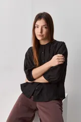 Camisa negra de textura liviana con detalle de lunares en relieve, cuello mao y cierre frontal con botones. Presenta mangas 3/4 con puños elastizados y frunces en los hombros.