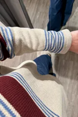 Sweater de punto corto con diseño a rayas horizontales en tonos beige, azul y bordó. Presenta cuello redondo y mangas largas con puños ajustados.