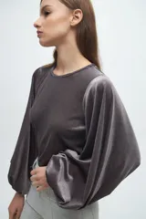 Blusa de terciopelo gris con acabado brillante, cuello redondo y mangas largas abullonadas con puños elásticos.
