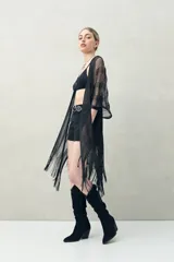 Poncho negro de tejido calado con flecos en el ruedo.