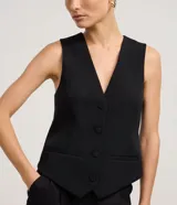 Chaleco negro de sastrería, corte slim, con escote en V profundo y cierre frontal de cuatro botones. Presenta bolsillos falsos o decorativos a la altura de la cadera.