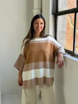 Poncho de punto con diseño de rayas horizontales en tonos tierra, blanco y beige. Presenta un corte holgado, cuello redondo y mangas anchas con puños acanalados.