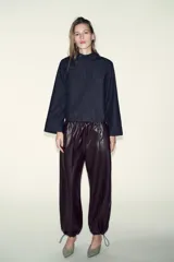 Camisa de denim azul oscuro, de corte cuadrado y manga ancha acampanada. Presenta cuello mao y cierre asimétrico con botones a presión en el frente.