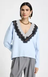 Sweater de punto color celeste con escote en V profundo, ribete acanalado gris y aplicación de encaje negro que delinea el escote. Presenta mangas largas con puños acanalados y dobladillo acanalado.