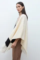 Ruana de tejido de punto con diseño color block en tonos crudo, gris y negro, con terminación de flecos en el ruedo y textura en relieve.