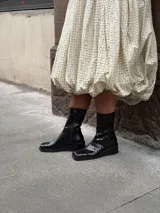 Bota de caña media con punta cuadrada y cierre lateral, confeccionada en cuero con textura croco y acabado charol negro.