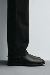 Bota estilo Chelsea de cuero negro con diseño liso, paneles elásticos laterales y tirador trasero. Presenta horma redonda y suela con tacón bajo.