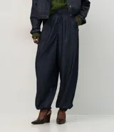 Pantalón de jean estilo aladín con cintura alta y pretina estructurada. Presenta pinzas frontales, volumen en la cadera y piernas con entalle progresivo que finalizan en puños con elástico, logrando un efecto jogger sofisticado.
