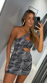 Vestido corto ajustado, negro con estampado geométrico de líneas plateadas brillantes. Diseño asimétrico de un solo hombro con un corte en la cintura.