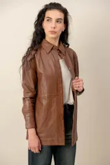 Campera estilo sobrecamisa confeccionada en cuero negro, de corte recto, con cuello camisero y cierre frontal de botones metálicos a presión.