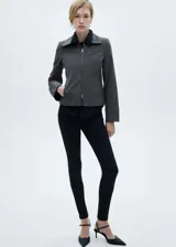 Chaqueta entallada de color gris con diseño de rayas verticales finas. Presenta cuello camisero, cierre frontal de cremallera doble y bolsillo de ribete en el pecho.