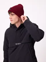 Gorro tipo beanie de punto acanalado en color bordó, con etiqueta de la marca Rusty en el frente.