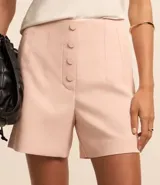Short de sastrería color rosa pálido, tiro alto, con cierre frontal simulado por una hilera de botones redondos del mismo color. Corte recto y estructurado.