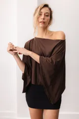 Blusa fluida de color marrón, con diseño holgado, escote bote que deja un hombro al descubierto y mangas anchas y cortas.