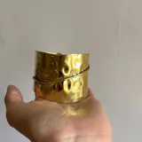 Brazalete rígido dorado con textura martillada y diseño envolvente.