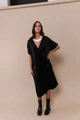 Vestido negro de corte midi, con escote en V y mangas cortas amplias. Presenta un cuello blanco con volados.