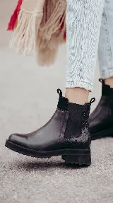 Bota tipo Chelsea de cuero negro con paneles elásticos laterales y suela track dentada. Presenta un diseño minimalista con tirador en la parte trasera.