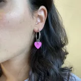 Par de aros plateados tipo argolla con dije de corazón rosa chicle.