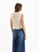 Chaleco color beige confeccionado en tejido semiliviano de galga 12, con calce regular, largo hasta la cadera y escote redondo clásico. Su diseño presenta una trama texturada con figuras geométricas.