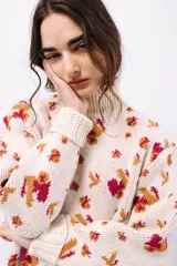 Polera de tejido de punto con cuello alto, diseño holgado y estampado jacquard con motivos geométricos y figuras en tonos beige, naranja y celeste.