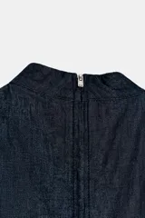 Vestido midi de denim oscuro con cuello perkins y diseño sin mangas. Presenta un corte entallado en el torso con una costura diagonal en la cintura y falda acampanada en línea evasé. Cierre posterior con cremallera metálica.