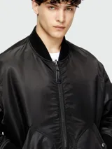 Campera bomber negra con acabado satinado, cierre frontal con cremallera y solapa con botones a presión. Presenta cuello, puños y ruedo de tejido acanalado, y bolsillos laterales con cierre.