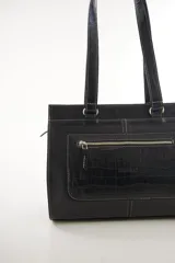 Cartera de cuero marrón de tamaño medio con diseño estructurado, que combina cuero liso y un panel frontal texturizado tipo cocodrilo con bolsillo exterior con cierre. Cuenta con doble asa de hombro y costuras visibles de contraste.