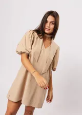 Vestido corto color beige, de corte oversize, con escote en V y mangas globo. Incluye cinturón marrón con hebilla dorada.