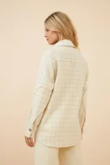 Camisa estilo leñador color beige con textura en espiga, de manga larga, con cuello clásico, cierre frontal con botones, dos bolsillos de parche con solapa abotonada en el pecho y puños abotonados. Confeccionada en lana fina sin teñir.