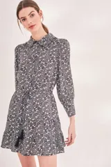 Vestido corto negro con estampado floral pequeño en blanco, cuello camisero, mangas largas abullonadas y cintura ajustable con lazo que termina en borlas negras.