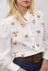 Camisa blanca de manga corta con cuello mao y volados, botones frontales y bordados de hojas y flores en color dorado.
