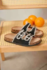Sandalias negras de dos tiras con hebillas metálicas y bordado blanco en los bordes, con suela estilo corcho.