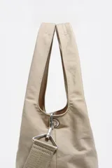 Bolso shopper de nylon color negro, con estructura blanda, doble asa de mano y correa ajustable extraíble. Presenta bolsillos laterales con cierre y logo metálico de la marca en la parte inferior.