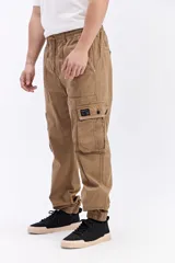 Pantalón cargo color tostado de corte amplio, con cintura elástica y cordón ajustable. Cuenta con bolsillos laterales con tapa en las piernas y puños elastizados en los tobillos.
