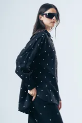 Camisa de corte clásico con estampa de lunares blancos sobre fondo negro, manga larga con puños abotonados y bolsillo frontal.