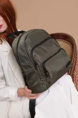 Mochila urbana de diseño funcional en color beige, confeccionada en tela impermeable. Cuenta con un compartimento principal amplio, un bolsillo secundario y un bolsillo frontal, todos con cierre. Incluye asa superior y correas ajustables para los hombros, con detalle de etiqueta de marca en el frente.