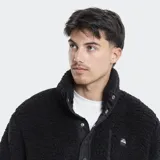 Campera de polar tipo borreguito color verde oliva, con cuello alto, cierre frontal parcial con botones a presión y bolsillo en el pecho con cierre. Presenta detalles en color beige en la solapa y los bordes.