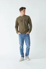 Remera verde militar de manga larga con cuello redondo y estampado frontal con la frase "Create the adventure".