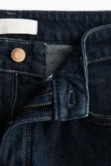 Jean de tiro alto con corte wide leg, confeccionado en denim de algodón con leve stretch. Presenta diseño clásico de cinco bolsillos, cierre frontal con botón y costuras en contraste.