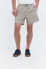Short de baño oversize color beige, con textura sutil, cintura elástica ajustable con cordón y bolsillos laterales. Presenta un pequeño estampado circular en la pierna izquierda.