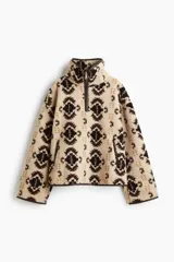 Buzo oversized de sherpa suave en color beige con estampado geométrico en tonos marrones y detalles en tejido revestido. Presenta cuello elevado, medio cierre frontal y bolsillos laterales.