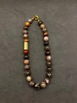 Collar de cuentas de piedras naturales en tonos tierra, con detalles de tubos dorados en los laterales.