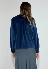 Chaqueta azul marino de terciopelo con cuello camisero, cierre frontal con botones, dos bolsillos de parche con solapa y mangas largas con puños abotonados.