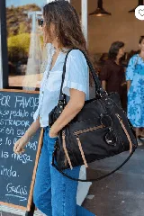 Bolso tote negro de cuero con herrajes y cierres metálicos. Presenta múltiples bolsillos exteriores con cierres y tiras decorativas de cuero en tono claro. Incluye asas de mano y una correa larga ajustable para llevar al hombro.
