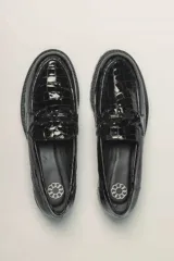 Mocasines negros de cuero vacuno con acabado charol, suela de goma y detalle de hebilla metálica.