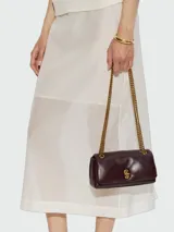Cartera Marc Jacobs modelo The Puffy Smooth Dual Chain Mini Bag, confeccionada en cuero liso de color bordó, con diseño acolchado y solapa frontal. Cuenta con cierre de broche metálico dorado y correa de cadena metálica doble.
