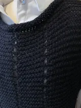 Chaleco negro de alpaca tejido a mano, ligeramente oversize, con hombros anchos, cuello tipo bote, puntos calados en frente y espalda, y tajos laterales en el bajo.