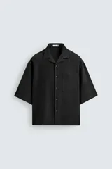 Camisa de corte boxy fit confeccionada en tejido con lino, color negro. Presenta cuello bowling, manga corta y un bolsillo plastrón en el pecho con cierre frontal de botones.